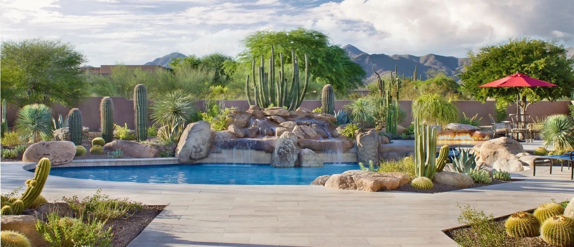 A pool with a waterfall and cactus in the background.