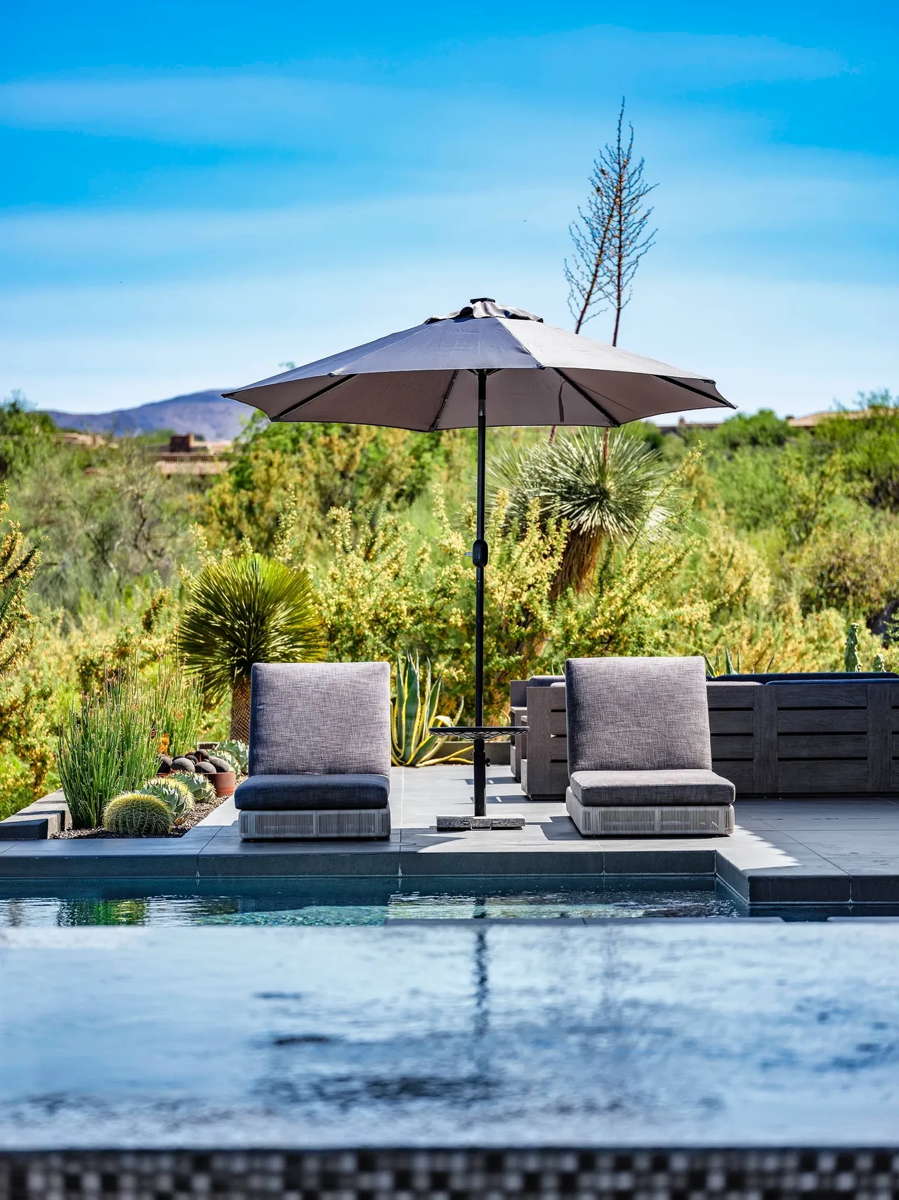 A couple of chairs and an umbrella by the pool.