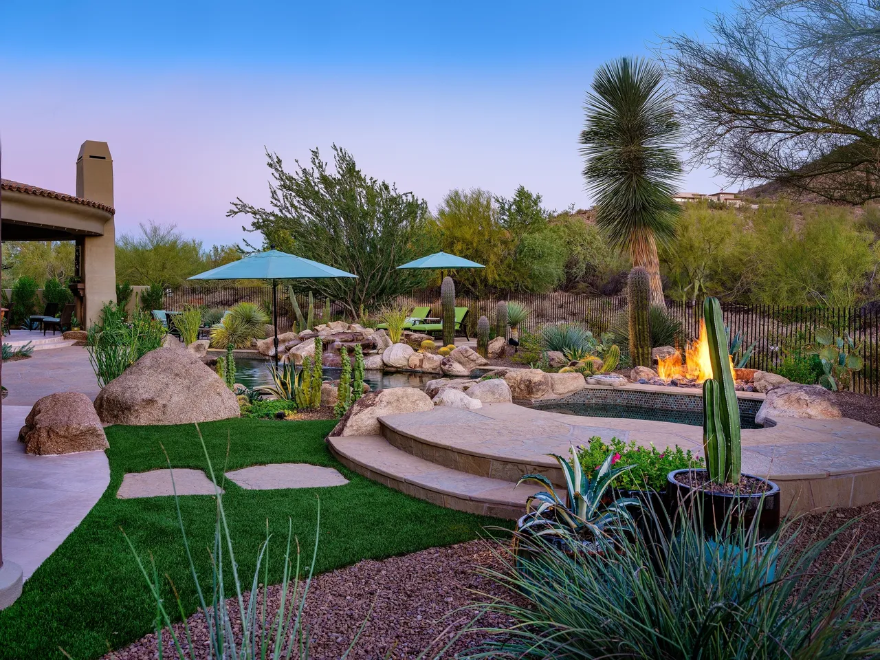 A backyard with fire pit, patio umbrellas and plants.