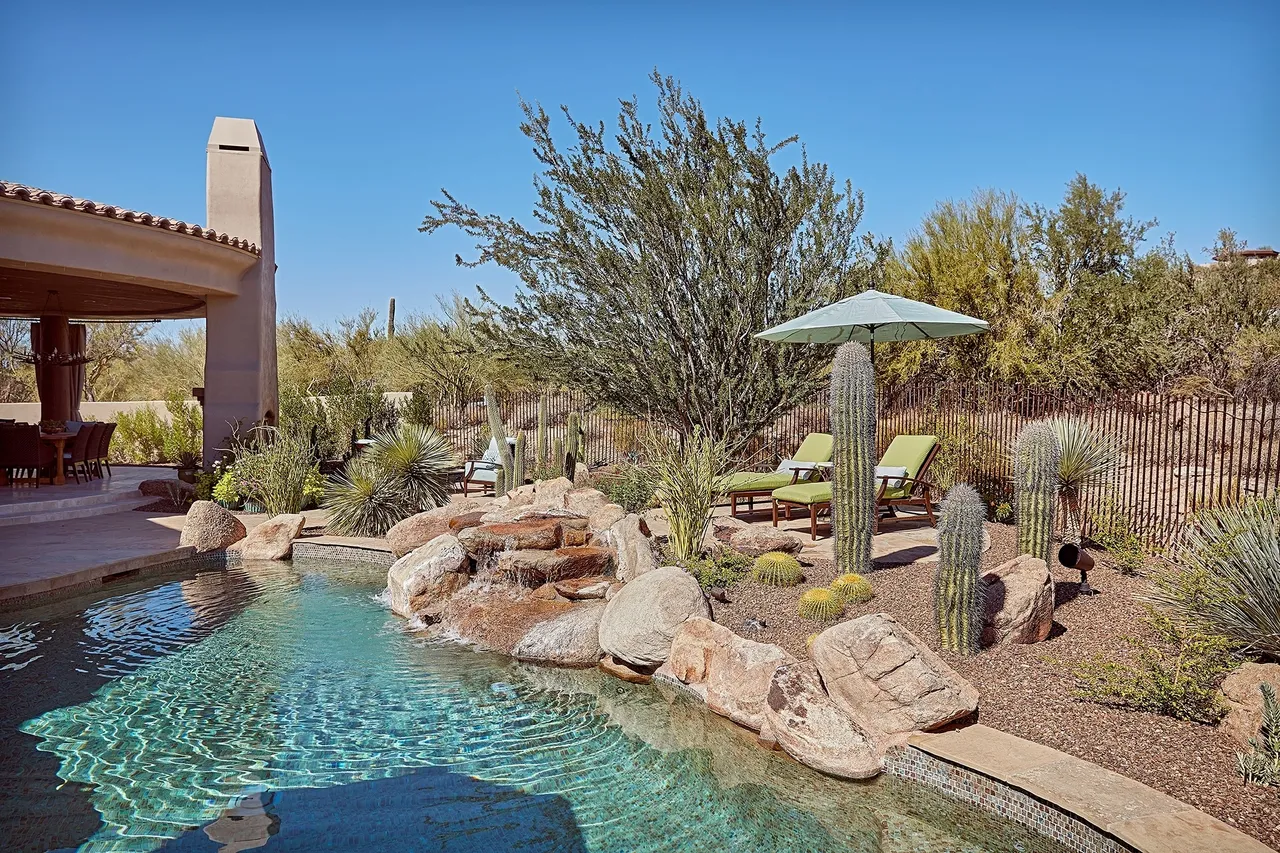 A pool with a large rock garden and patio furniture.