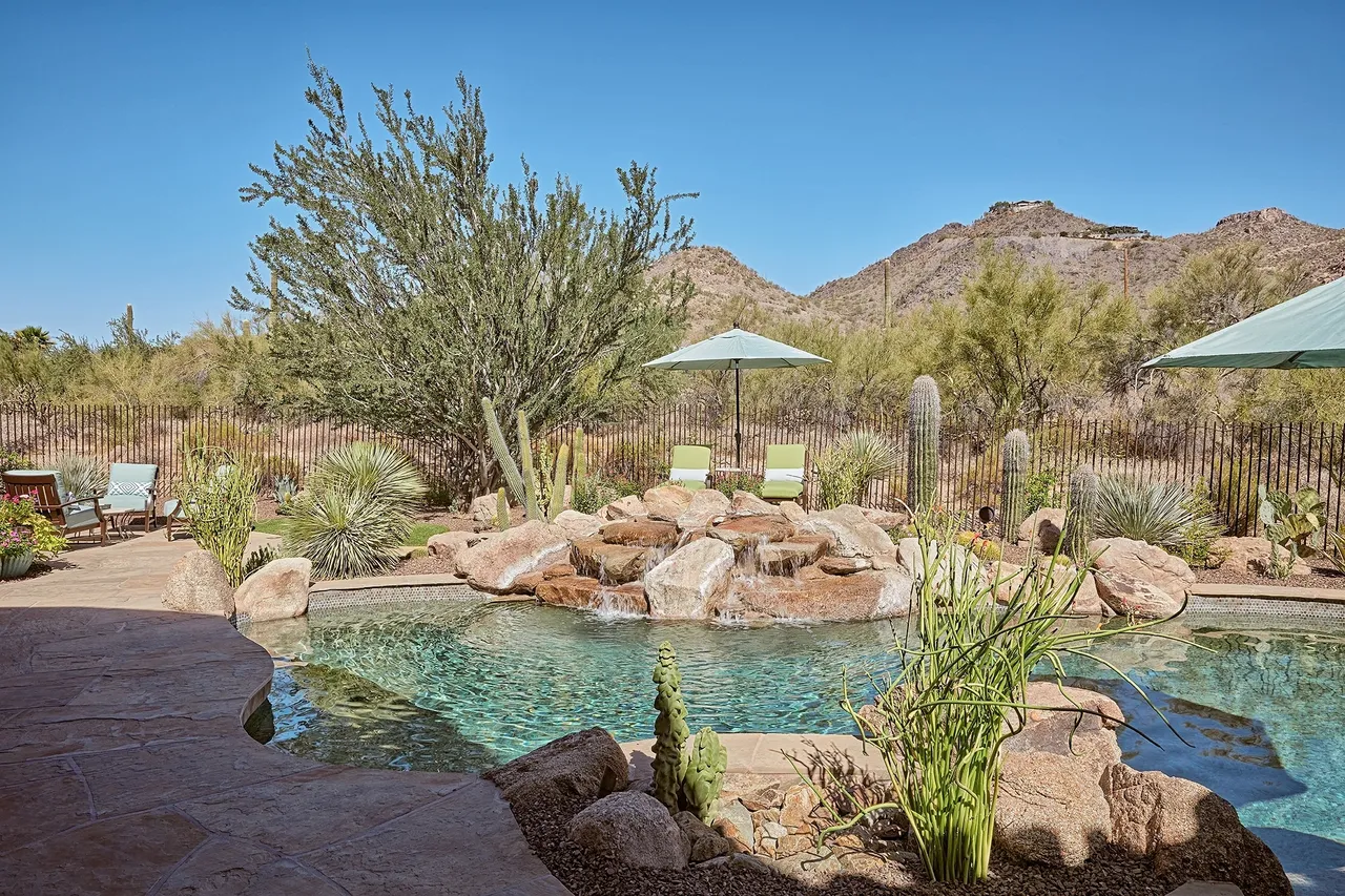 A pool with a rock garden and a blue umbrella.