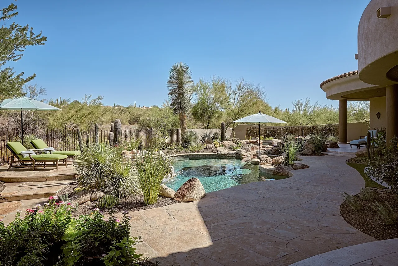 A pool with a waterfall and a gazebo in the middle of it.