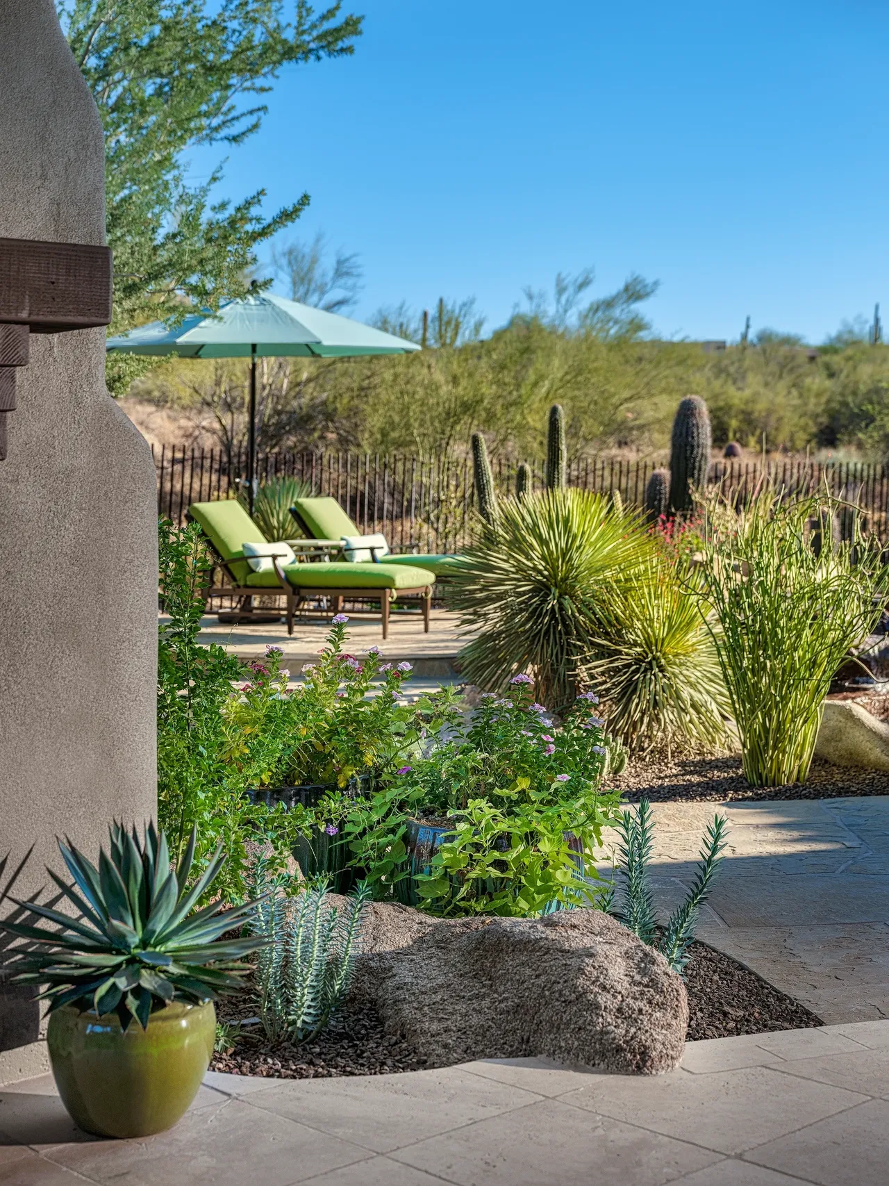 A patio with chairs and an umbrella in the middle of a garden.