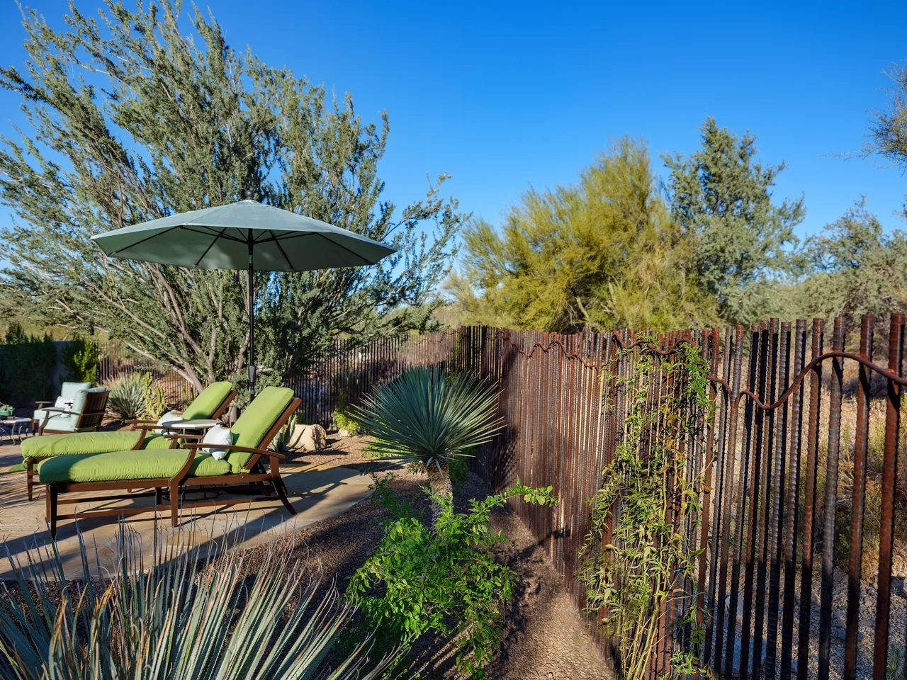 A patio with an umbrella and chairs in the middle of a yard.