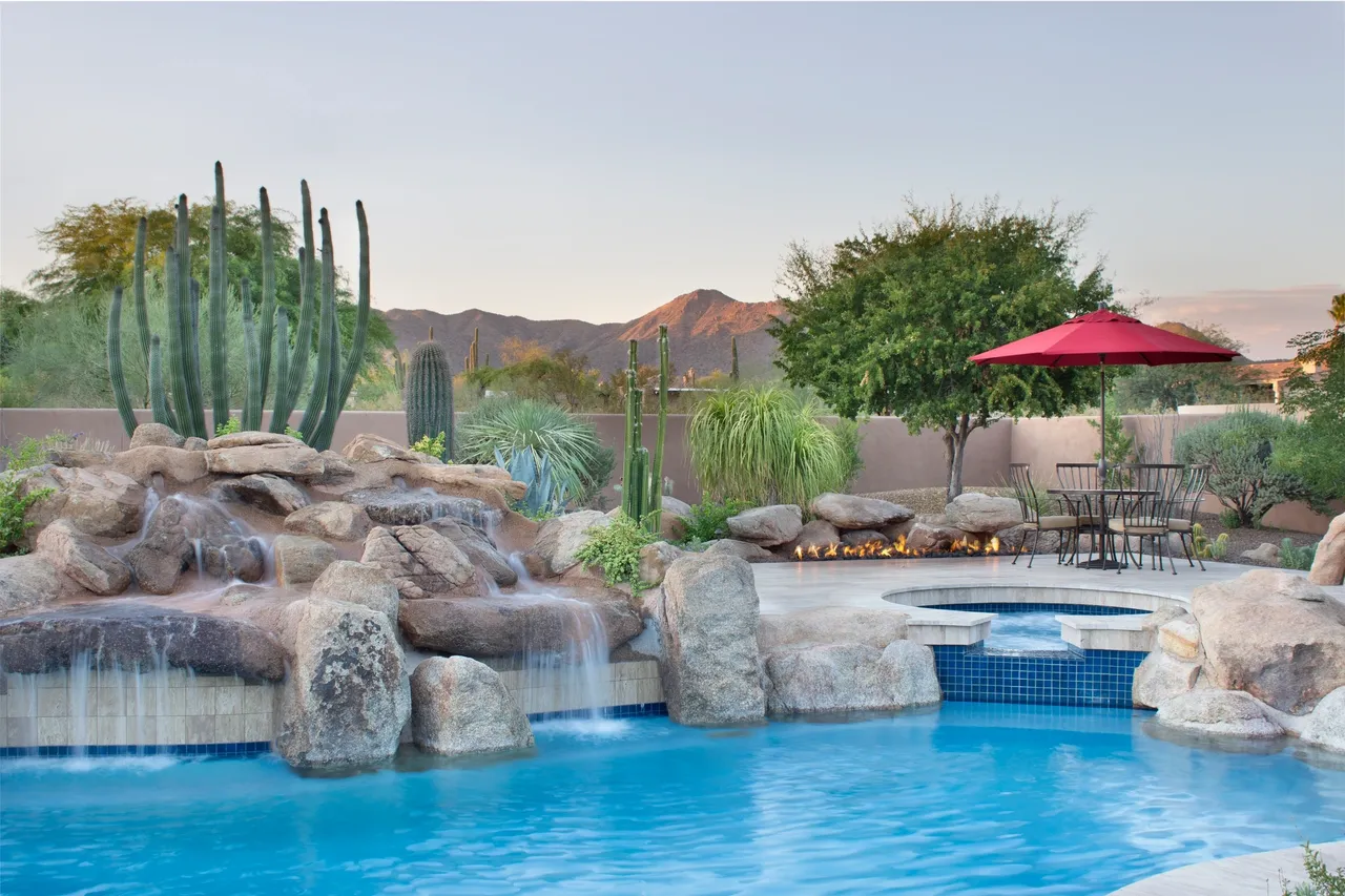 A pool with a waterfall and a red umbrella.