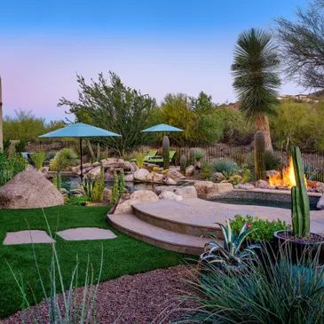 A backyard with fire pit, palm trees and grass.