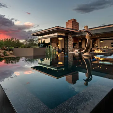 A pool with a fountain and a house in the background.