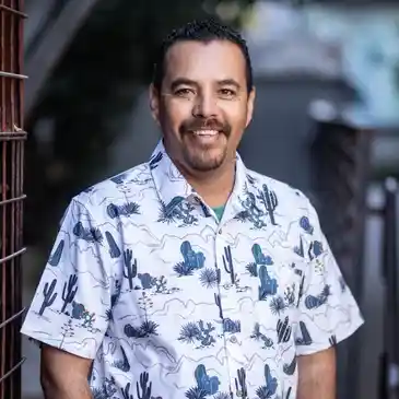 A man in a cactus shirt standing next to a fence.