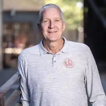 A man standing in front of stairs wearing a white shirt.