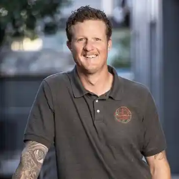 A man with tattoos standing in front of trees.