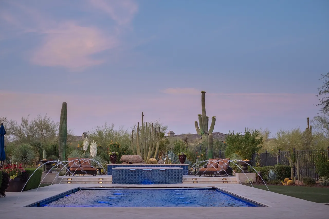 A pool with a fountain and cactus in the background.