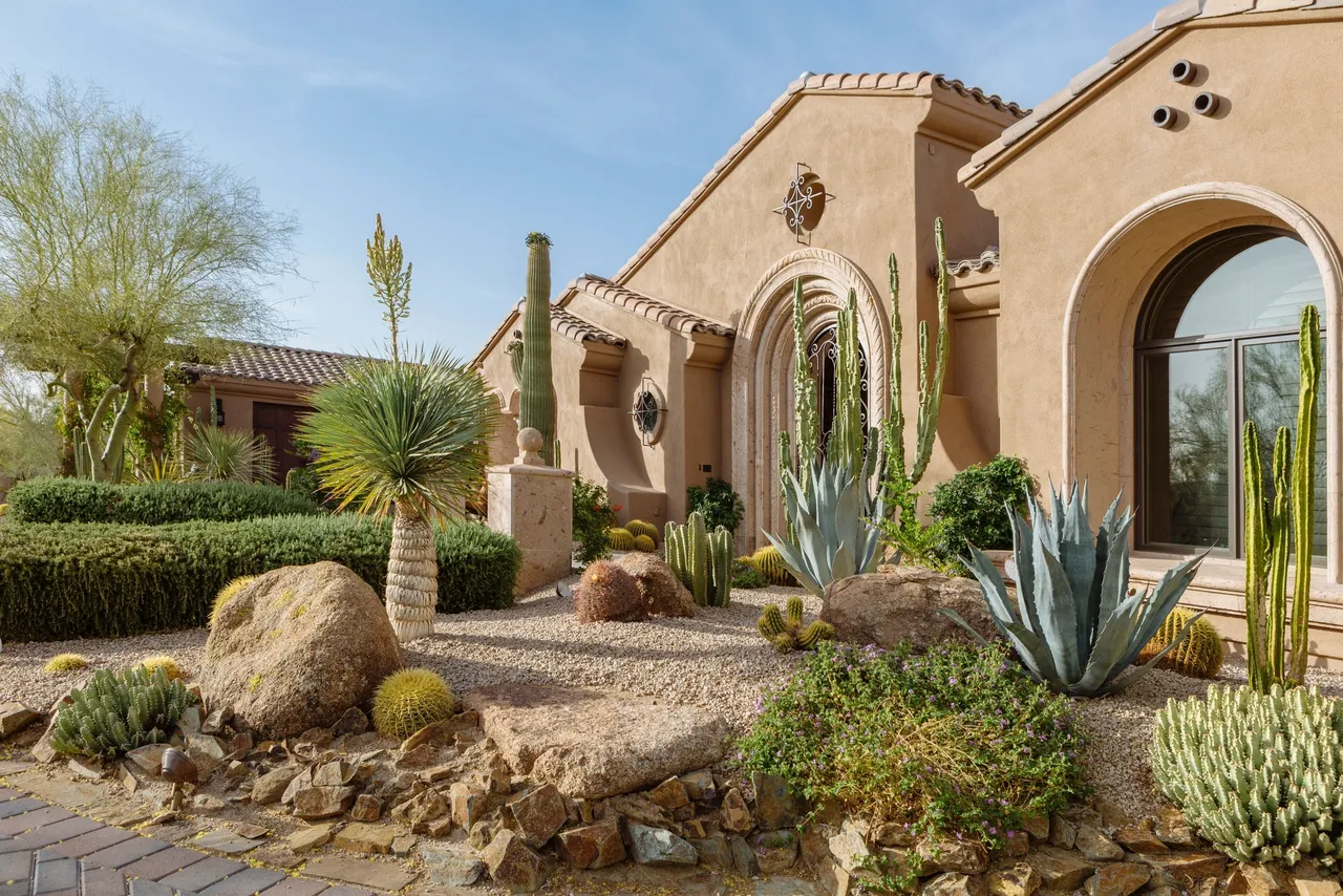 A desert style home with cactus and palm trees.