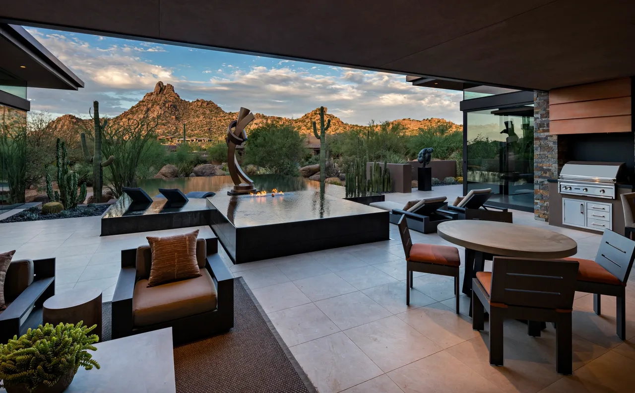 A patio with tables and chairs, a statue of a man in the middle of the desert.