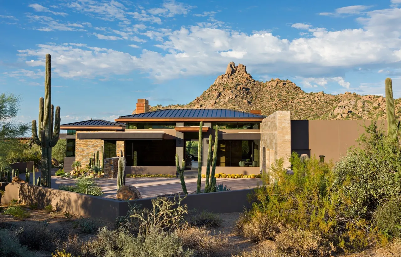 A house with a large roof in the middle of a desert.