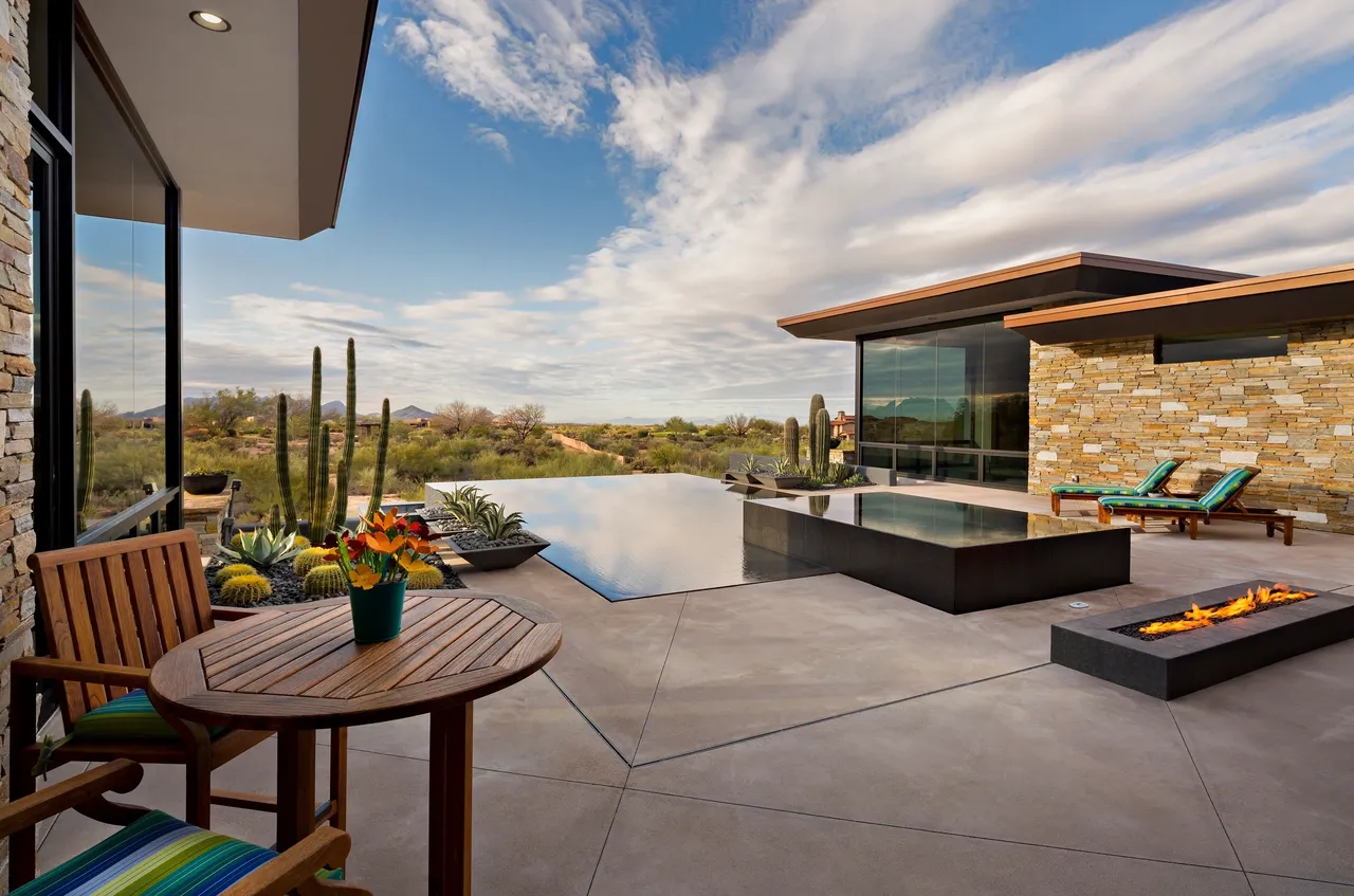 A patio with a table and chairs, pool and hot tub.