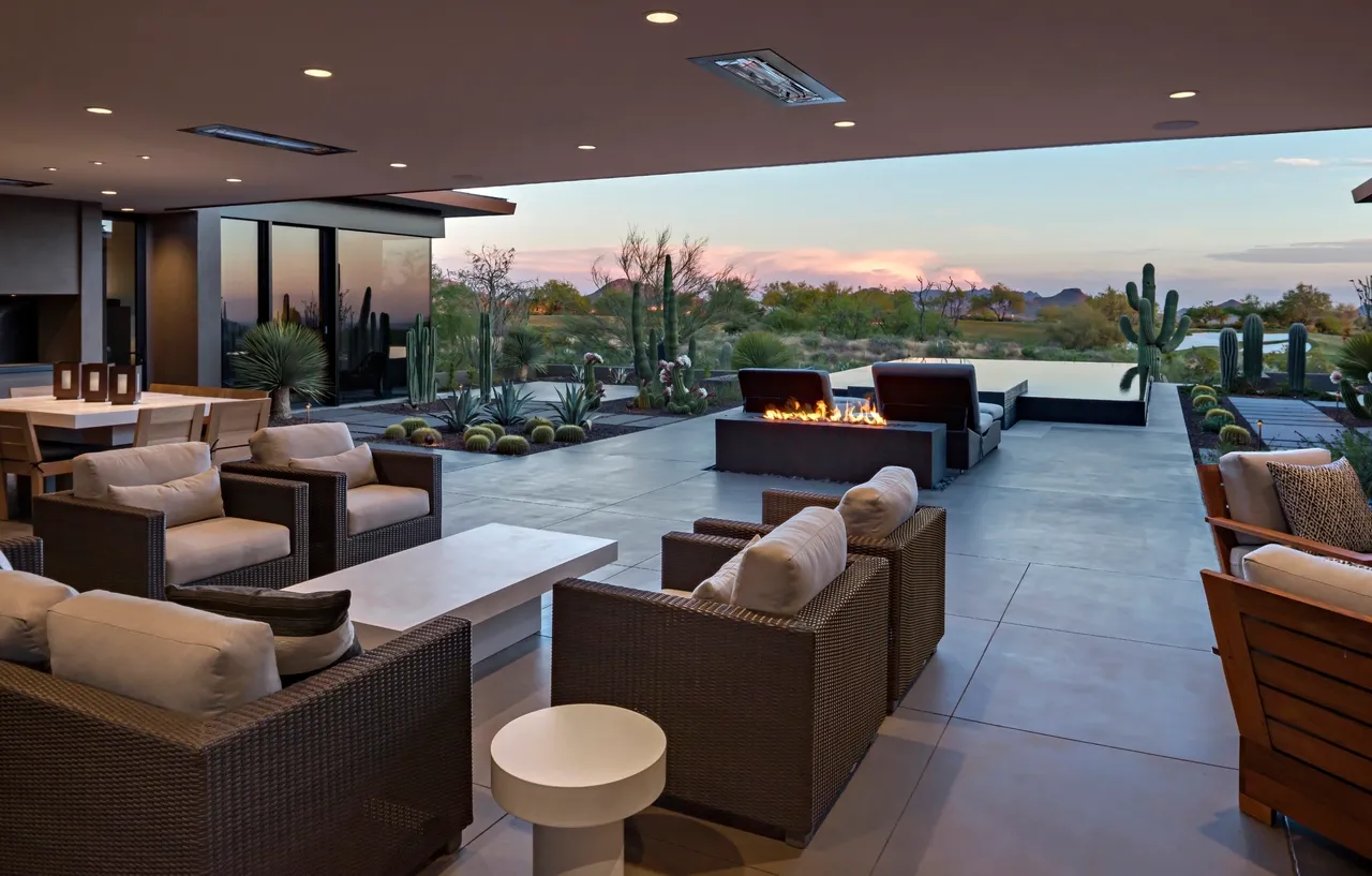 A patio with couches and tables in front of an outdoor fire pit.