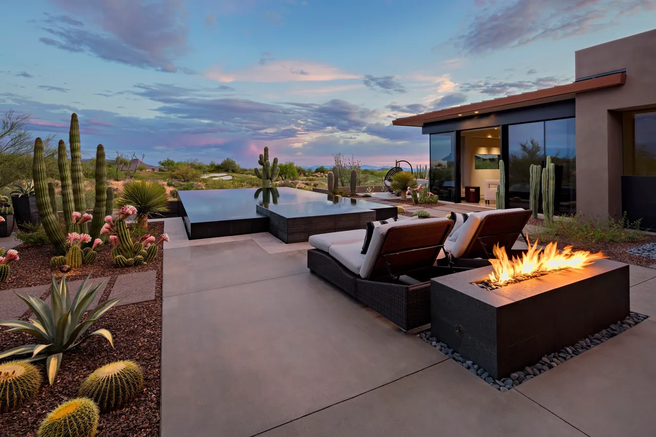 A patio with fire pit and lounge chairs.