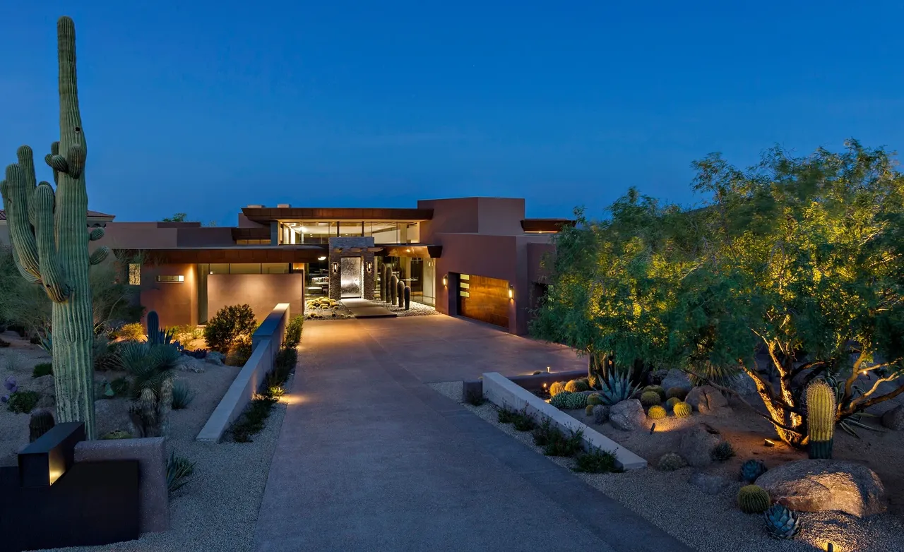 A large house with a driveway and lights on.