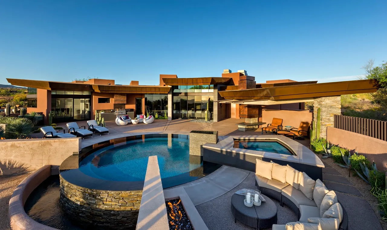 A large pool with a fire pit and lounge chairs.