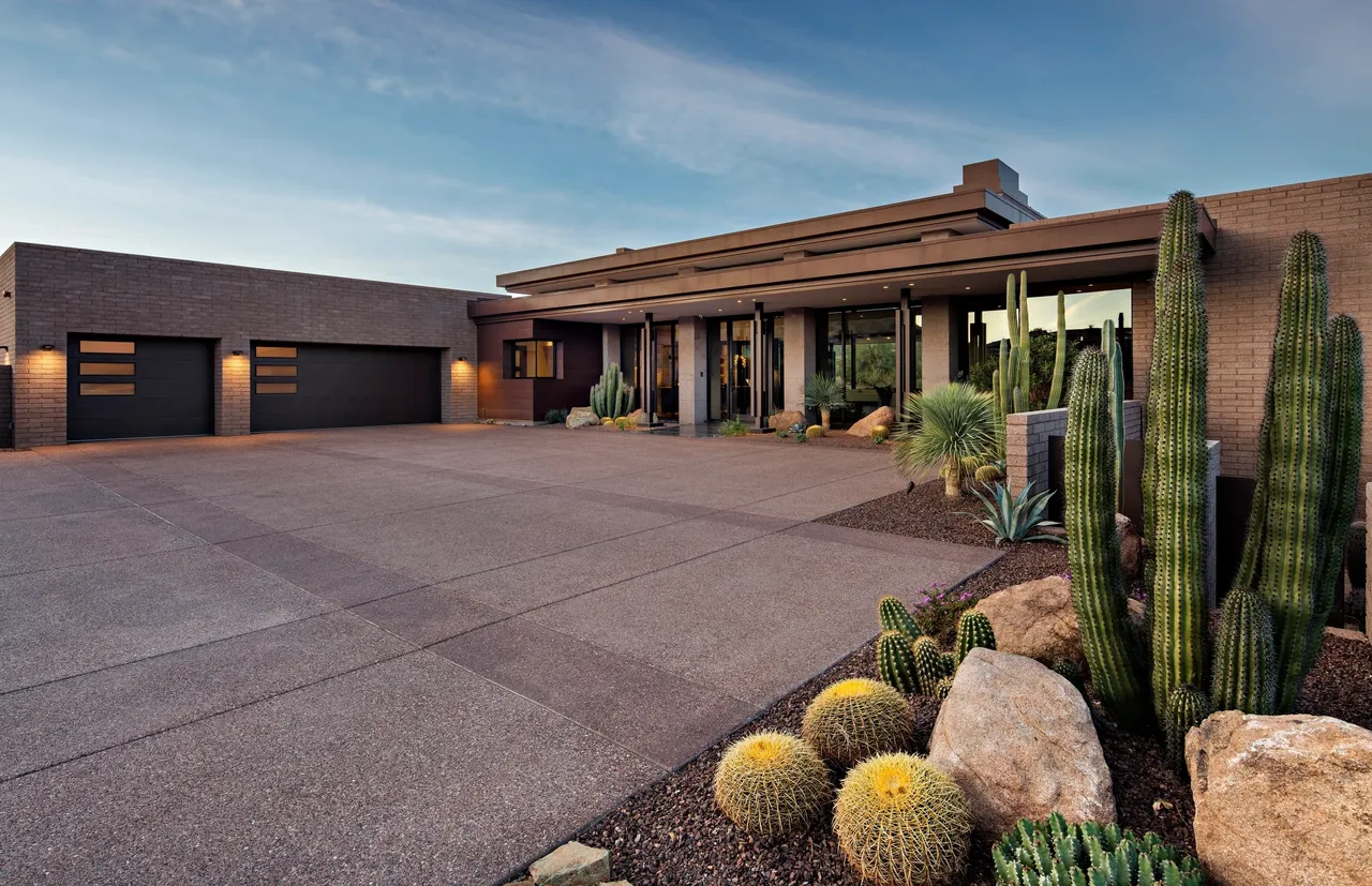 A large driveway with cacti and bushes in the front.