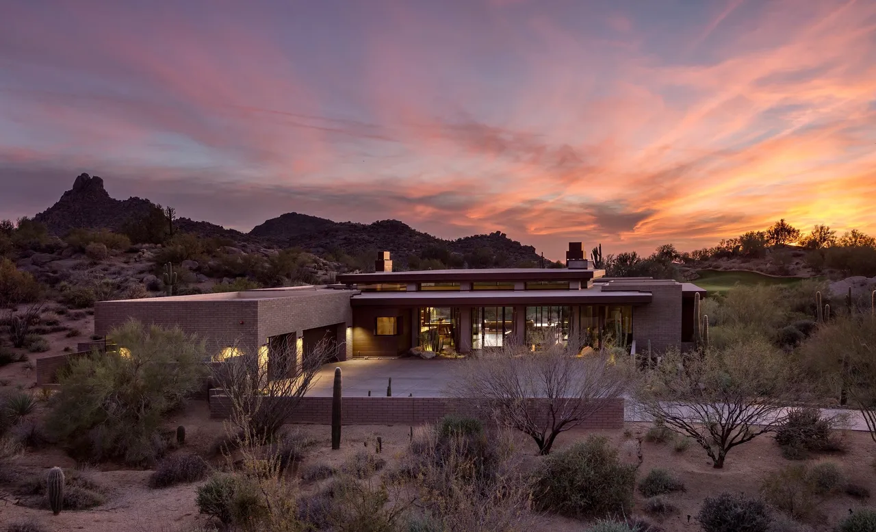 A large modern house with a sunset in the background.