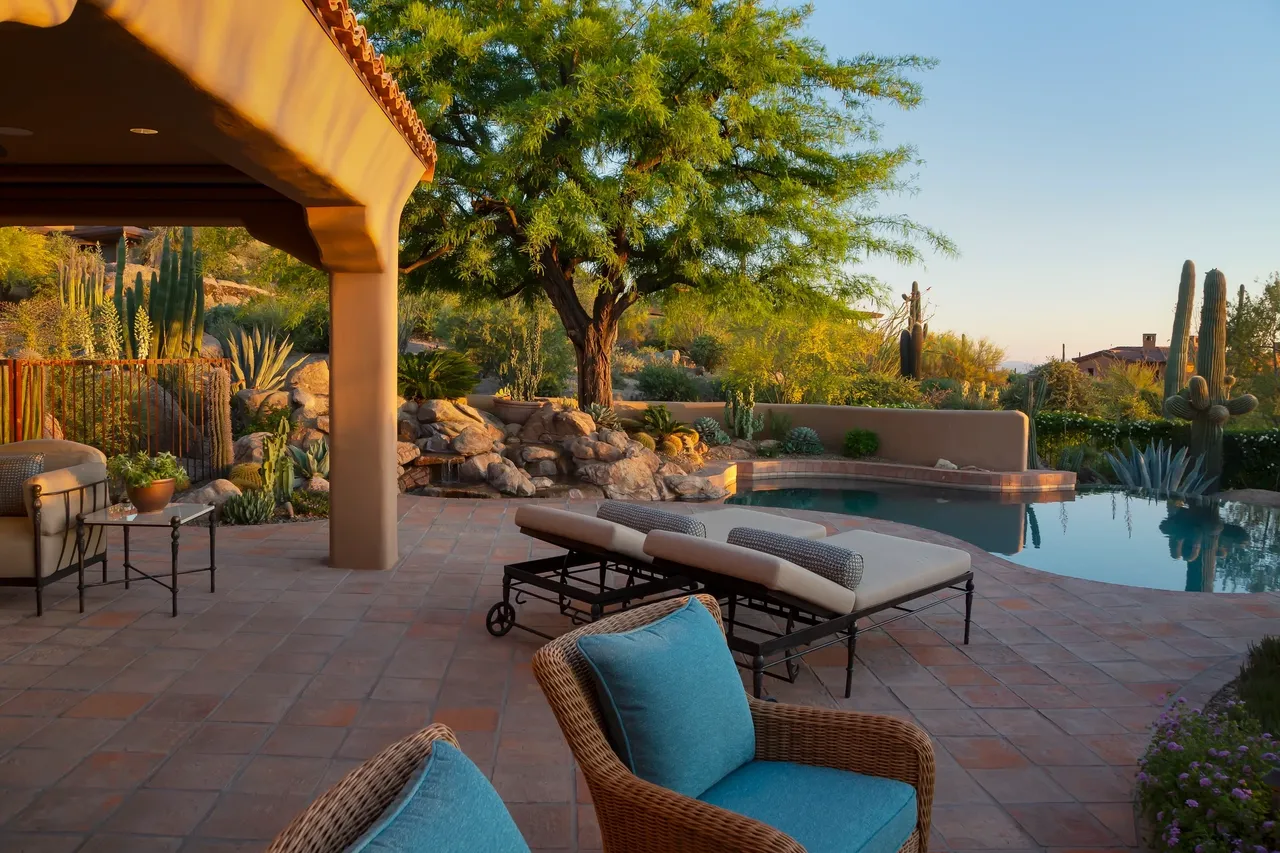 A patio with chairs and a pool in the background.