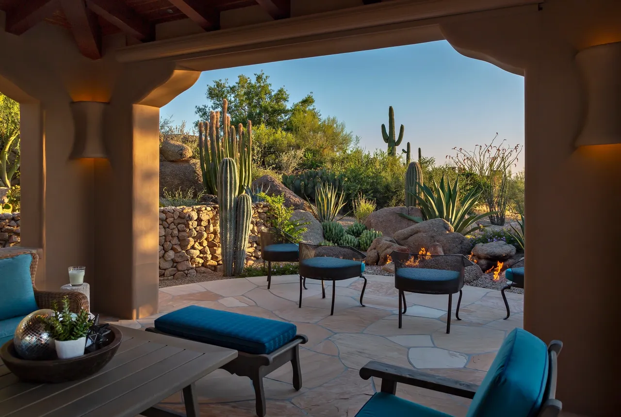 A patio with blue chairs and benches in the middle of a garden.